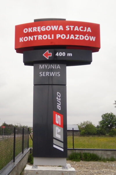 Znak drogowy wskazujący kierunek do Okręgowej Stacji Kontroli Pojazdów i myjni serwisowej.