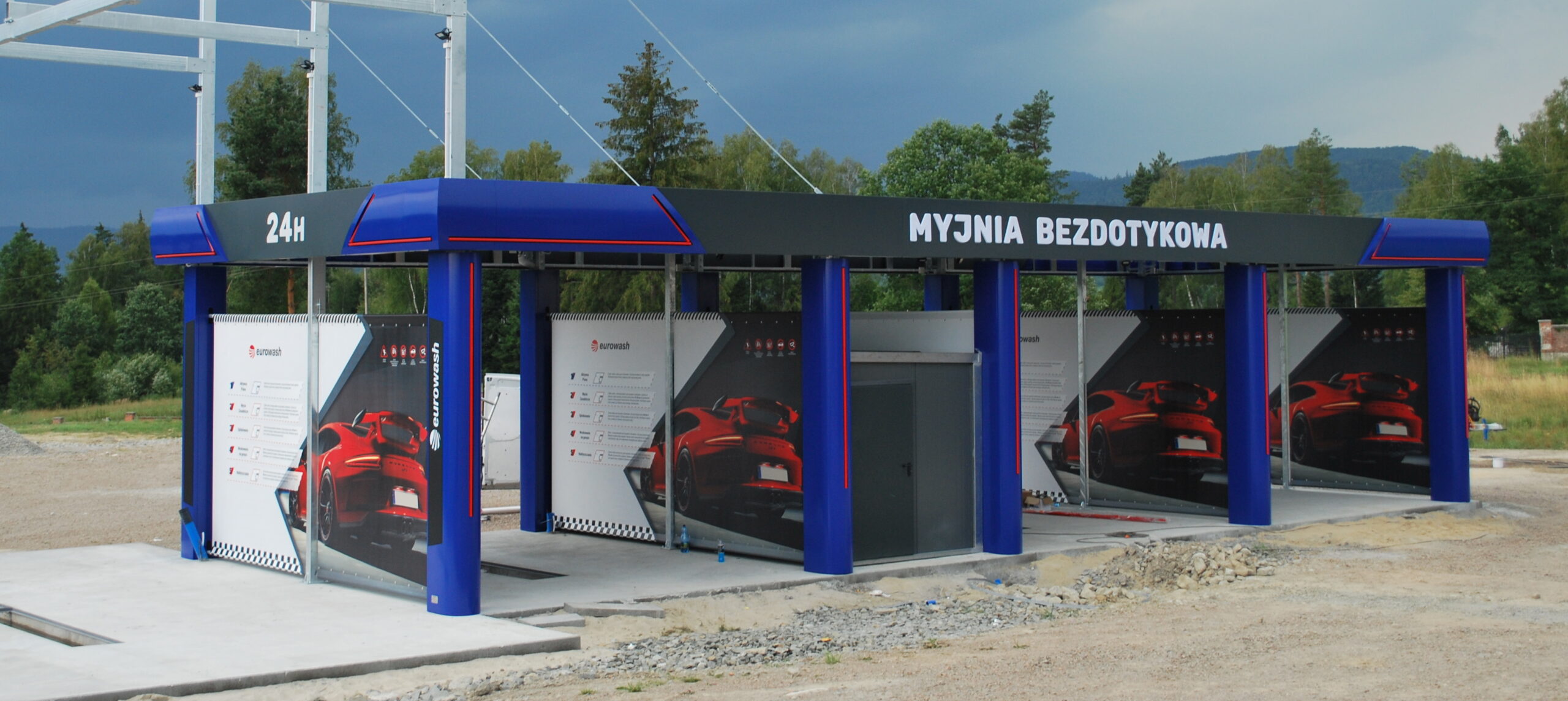 Bezdotykowa myjnia samochodowa z czerwonymi samochodami na zewnętrznych ścianach.