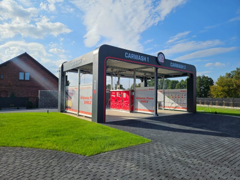 Widok na nowoczesną automatyczną myjnię samochodową z oznaczeniami 'CARWASH 1' i 'CARWASH 2'.