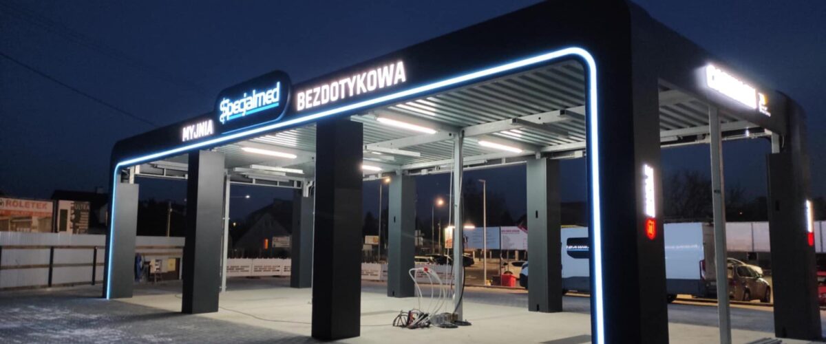 Bezdotykowa myjnia samochodowa z podświetleniem w nocy, z widocznymi stanowiskami do mycia.