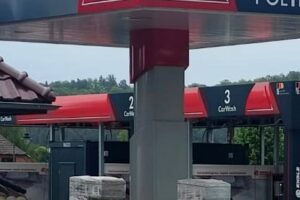 Stacja paliw z dystrybutorami paliwa i myjnią samochodową w tle.