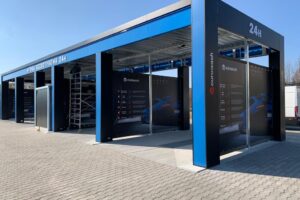 Automatyczna myjnia samochodowa z niebieskim dachem i informacjami na ścianach.